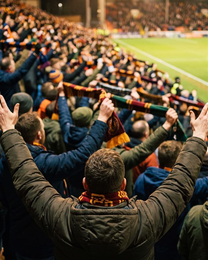 A packed stand with scarves held high and arms in the air