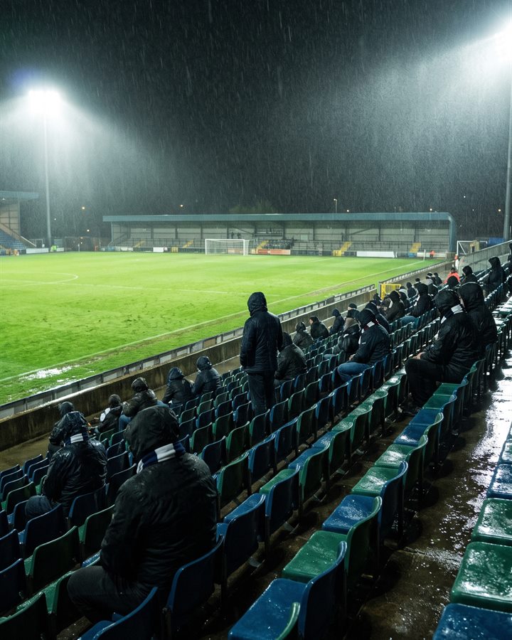 Supporters huddled in hoods in a near-empty stand as the rain pours down under the floodlights